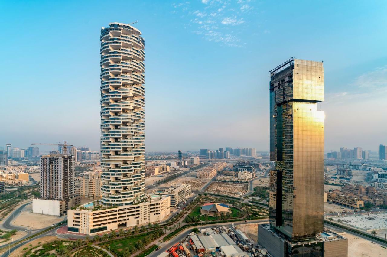 Five Jumeirah Village Дубай Экстерьер фото The photo shows two distinctive skyscrapers located in an urban area. On the left, there is a tall, cylindrical building with a unique, modern design characterized by its twisting, spiral shape and balconies at various levels. To the right, there is 